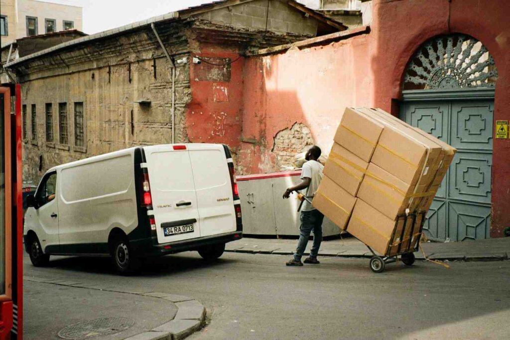 Delivery worker moving large boxes toward a van, illustrating the higher expenses and logistics challenges of offering free shipping for bulky products.
