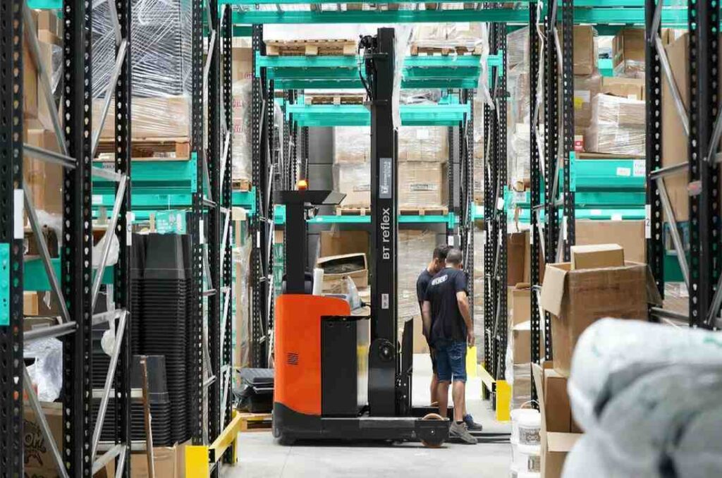 Warehouse workers operating a forklift among stacked boxes, symbolizing the logistics and shipping process behind the USPS vs FedEx comparison — highlighting the difference between FedEx and USPS delivery speed, reliability, and nationwide service.