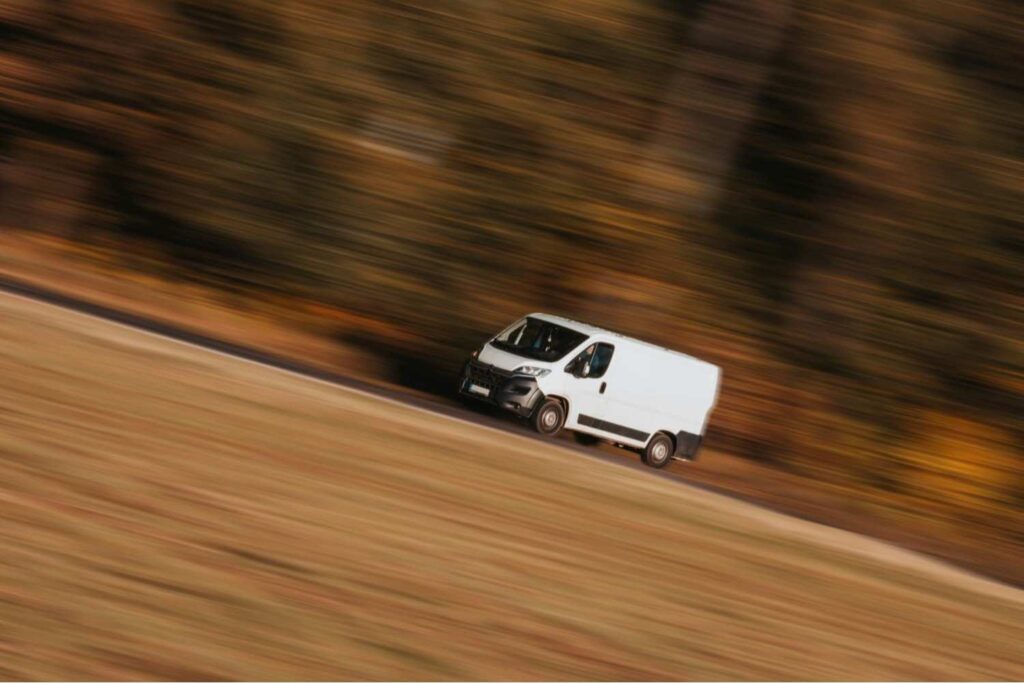 White delivery van speeding down a country road, symbolizing the urgency of USPS vs FedEx overnight shipping — representing the difference between FedEx Standard Overnight and USPS Priority Mail Express delivery speed and reliability.