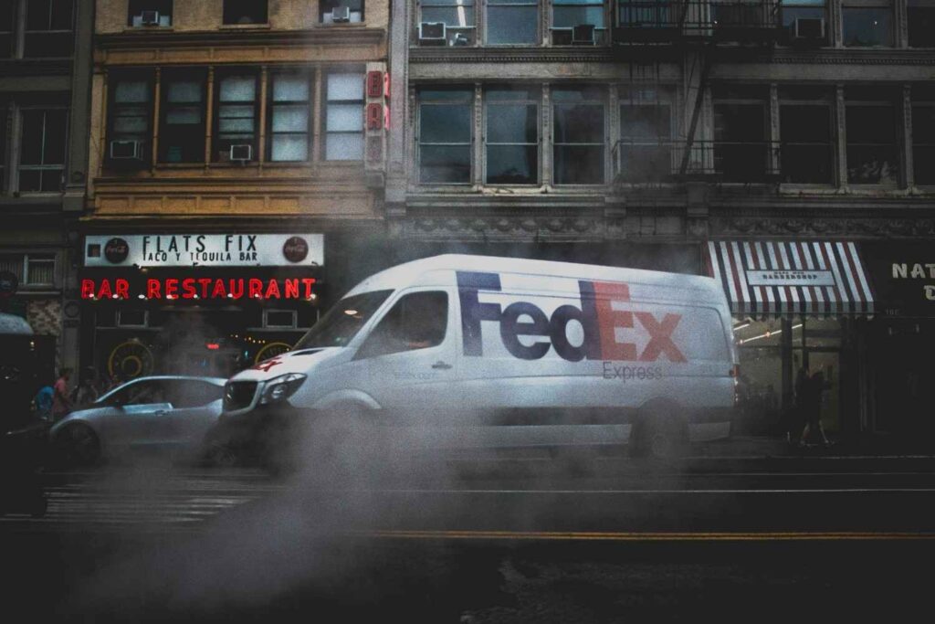FedEx Express delivery van driving down a city street, illustrating FedEx Ground service in the USPS vs FedEx comparison — highlighting the difference between FedEx and USPS delivery speed, reliability, and cost for ground shipping.