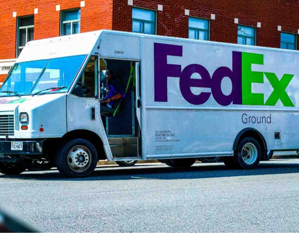 Delivery person in a green jacket standing beside a white and blue courier van, representing shipping services.