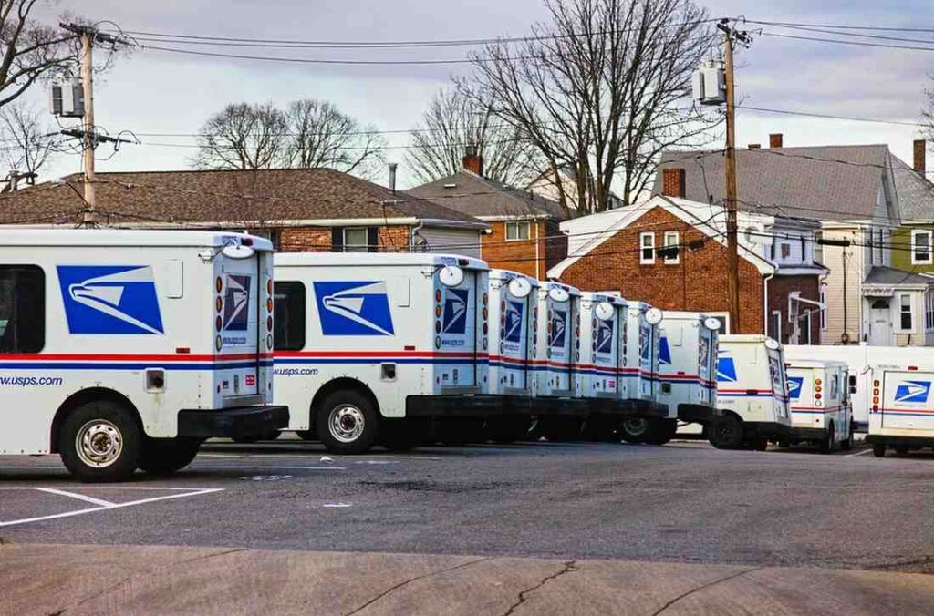 Row of USPS mail trucks lined up outside a post office, representing the USPS side of the USPS vs FedEx comparison — showing why shippers weigh FedEx or USPS for nationwide reliability, delivery coverage, and affordability.