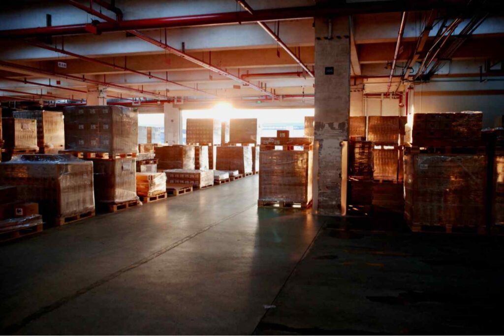 Warehouse filled with stacked pallets of packages at sunrise, representing the key differences between FedEx and USPS shipping operations, logistics speed, and nationwide delivery services in the ongoing USPS vs FedEx comparison.